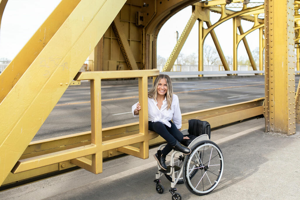 alycia sitting on the rails of the golden bridge in downtown sacramento smiling out of her wheelchair