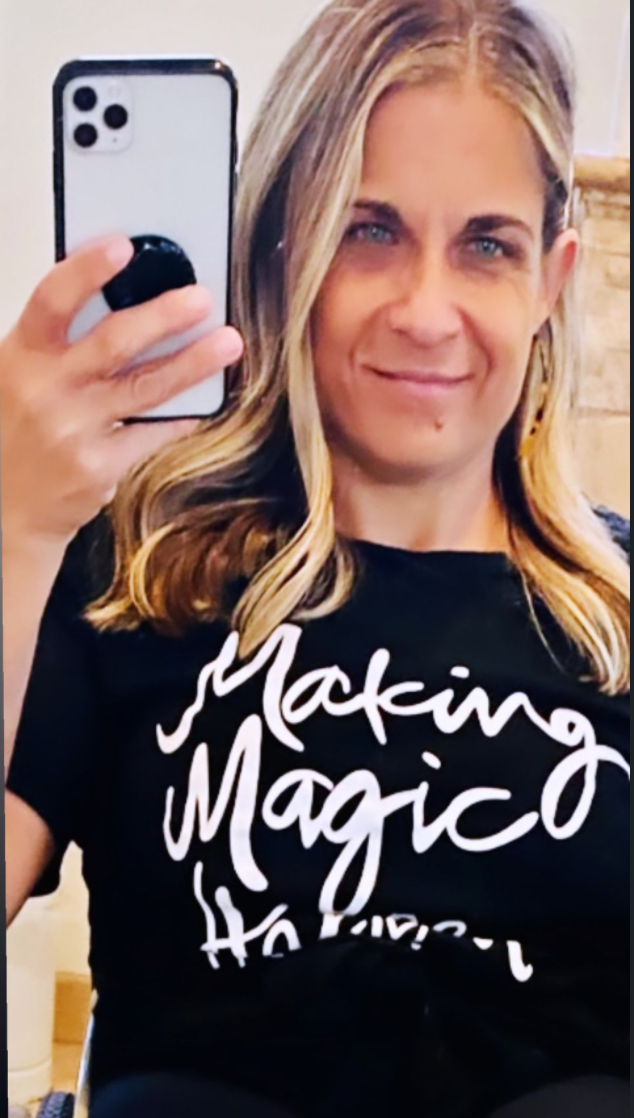 alycia holding her phone wearing a shirt that says making magic happen