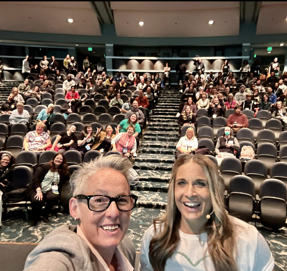 Alycia and Tonya on stage with crowd behind us doing a selfie right before Alycia takes the stage.